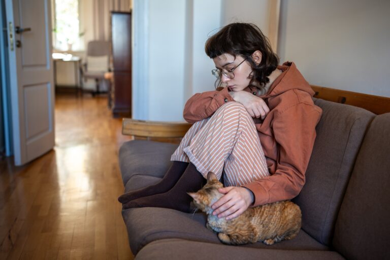 Depressed exhausted teen girl petting cat sitting on couch at home. Mental problem, pet therapy.