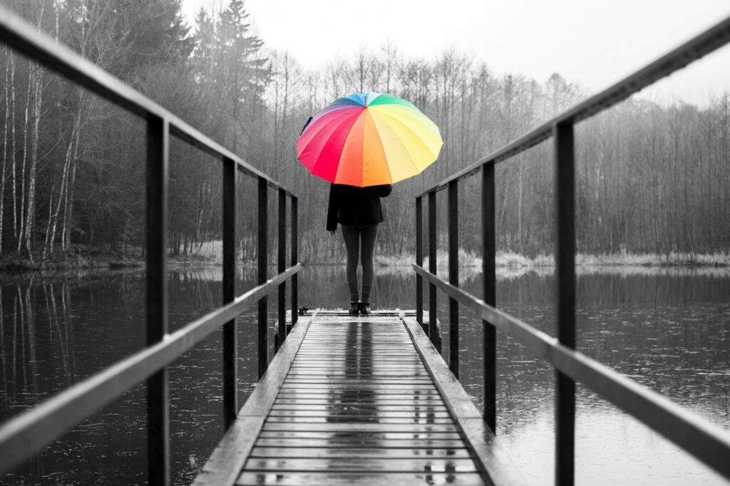 Woman standing with colorful umbrella on the pier at the pond on a rainy day